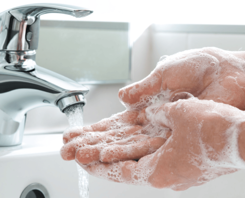 Primer plano de las manos de una persona siendo lavadas con jabón en el grifo del baño