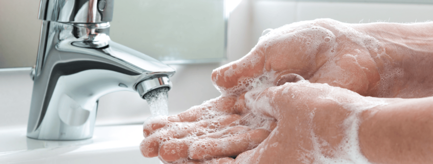 Primer plano de las manos de una persona siendo lavadas con jabón en el grifo del baño